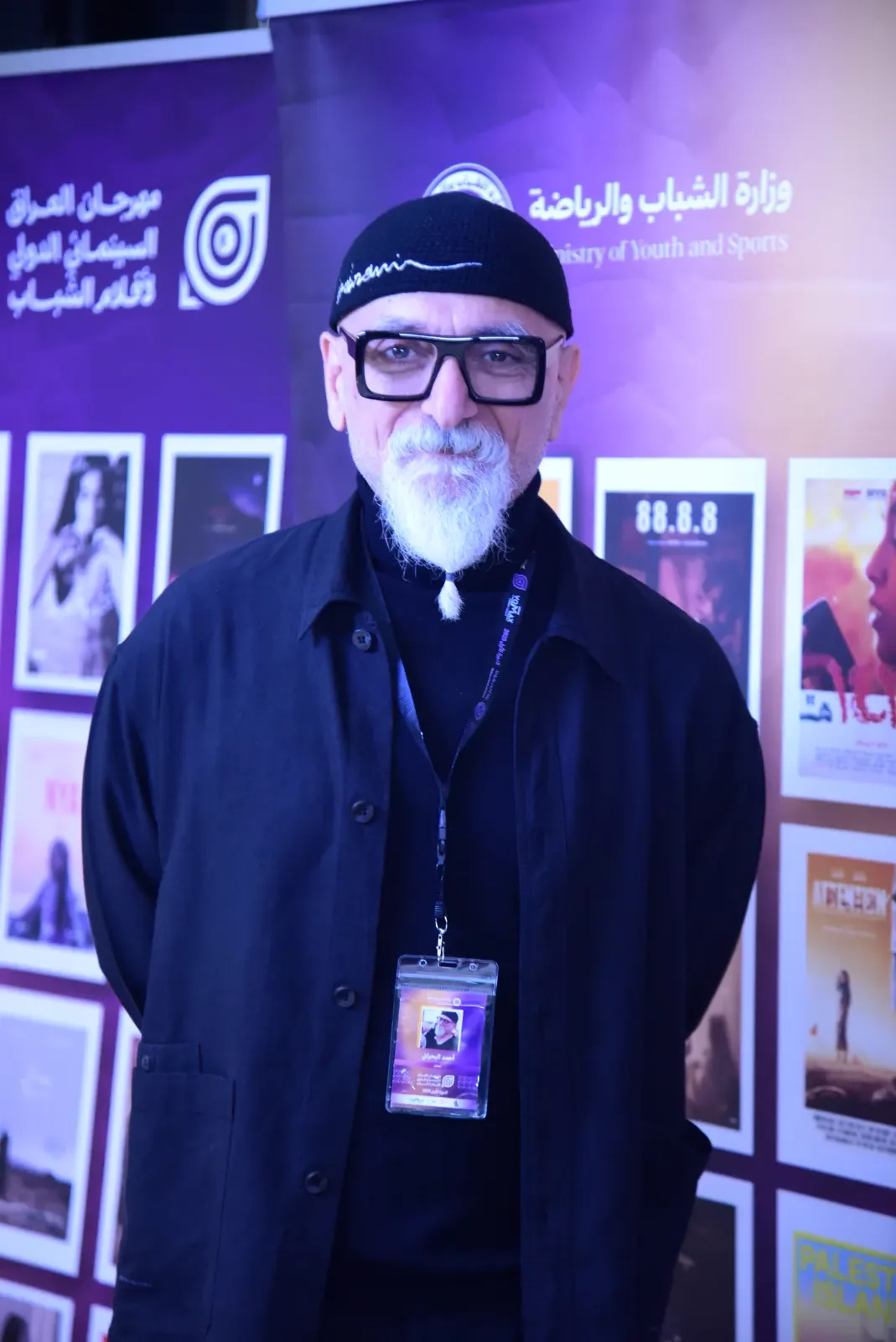 أحد ضيوف الدورة الأولى أمام جدار الملصقات